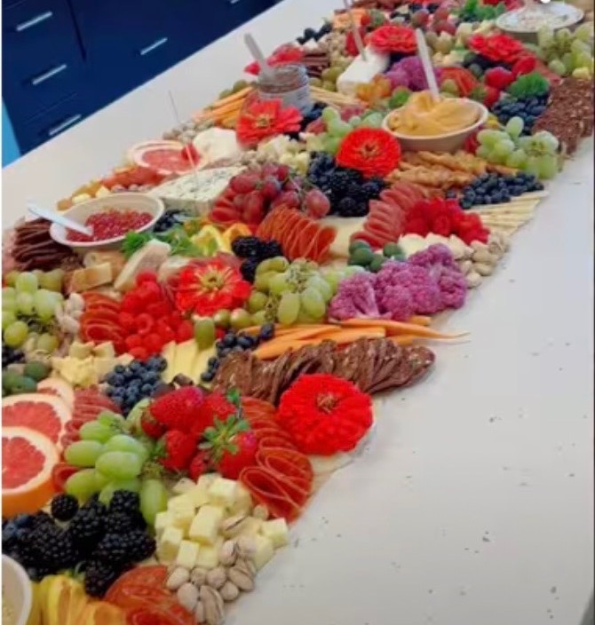 Grazing table with fruit, cheese, cured meats and red flowers